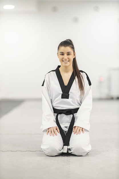 Photo fille sportive de taekwodno agenouillée à l'école d'arts martiaux préparée pour l'entraînement