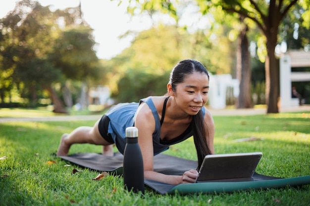 Fille sportive travaillant sur un tapis sur l'herbe dans le parc tout en utilisant une tablette