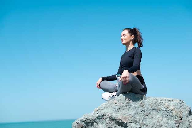 Fille sportive en vêtements de sport sur un rocher au bord de la mer