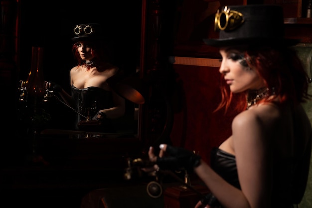 Fille steampunk dans la réflexion miroir Décolleté plongeant chapeau lunettes rondes et téléphone combiné