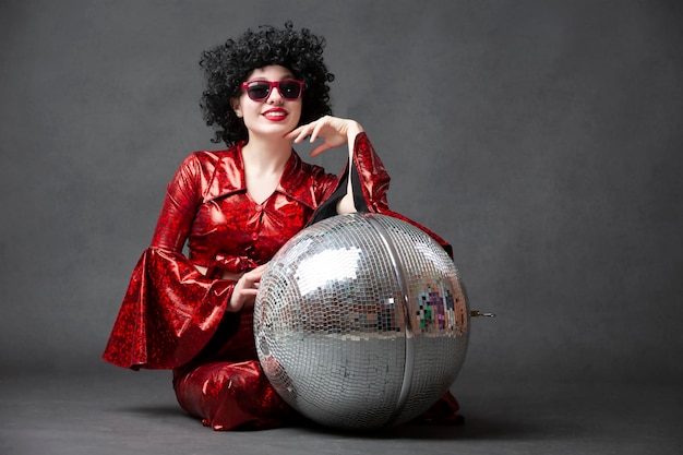Une fille de style disco dans un costume rouge brillant posant avec une balle disco