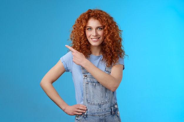 Une fille suggère une annonce pour un endroit parfait. Sassy belle femme audacieuse rousse habilitée souriante affirmée motivée pointant le coin supérieur gauche sourire à pleines dents confiant que vous aimez le fond bleu promotionnel.