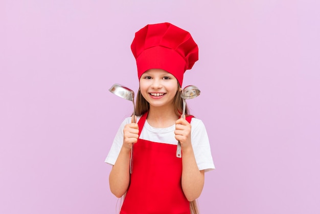 Une fille surprise dans un costume de chef rouge avec deux louches dans ses mains sur un fond violet isolé