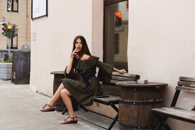 Fille surprise dans une robe légère assise sur le banc et regardant de côté.