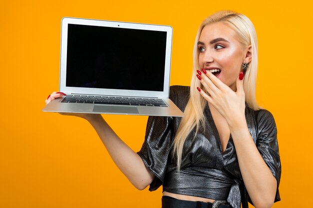 fille surprise détient un ordinateur portable avec un modèle de page web sur le mur jaune