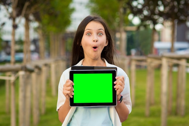 une fille surprise tient une tablette dans ses mains en plein air