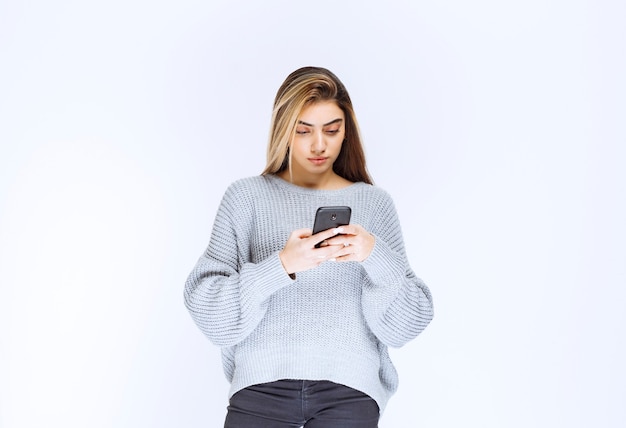 Fille en sweat-shirt gris tenant un smartphone noir et écrivant un message ou un commentaire.