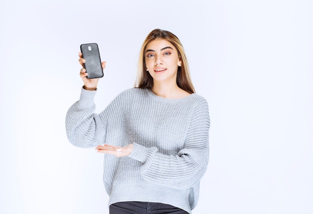 Fille en sweat-shirt gris tenant un smartphone noir.