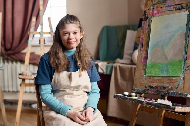 Photo une fille avec le syndrome de williams assise à côté d'un chevalet dans un studio d'art