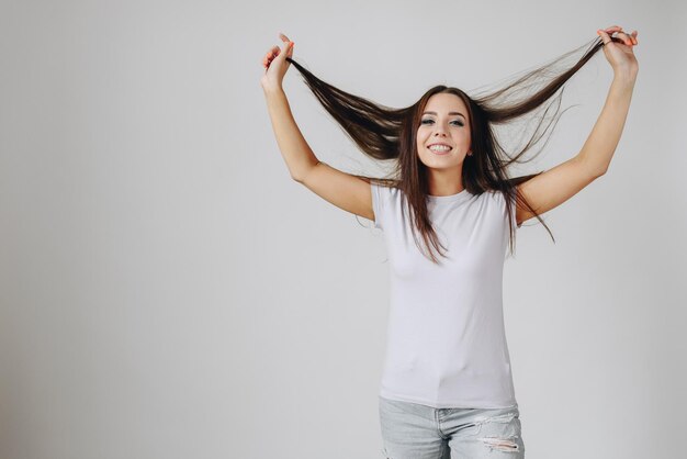 Fille en T-shirt blanc sur fond blanc lève ses cheveux et sourit joyeusement