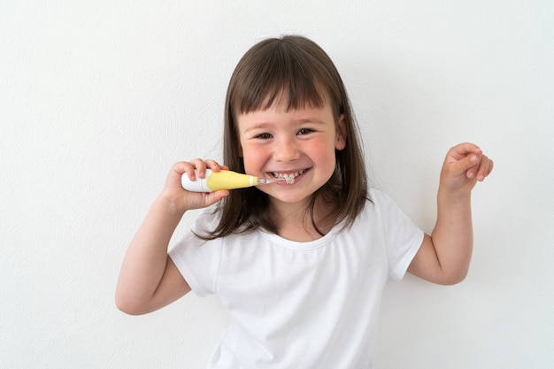 fille en t-shirt blanc se brosse les dents avec une brosse électrique