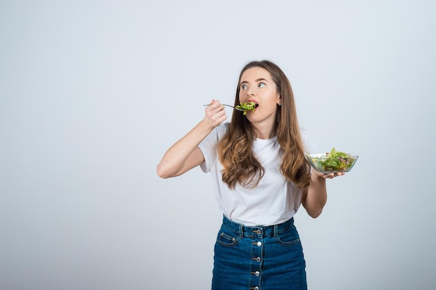 une fille en t-shirt blanc tient un bol de salade dans ses mains et mange