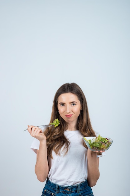 une fille en t-shirt blanc tient un bol de salade dans ses mains et mange