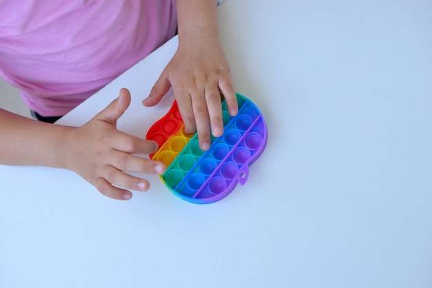 Une fille en t-shirt rose joue avec un jouet tendance pop it. jouet sensoriel anti-stress coloré fidget push pop it dans les mains des enfants, peut être utilisé pour s'entraîner avec des personnes autistes.