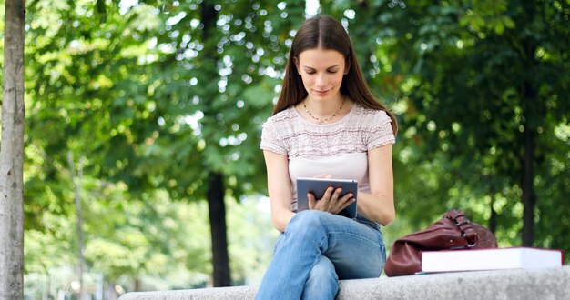 Fille avec tablette assis sur un banc de parc