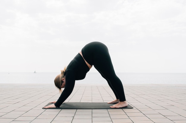 Fille de taille plus pratiquant le yoga devant l'océan un jour d'été