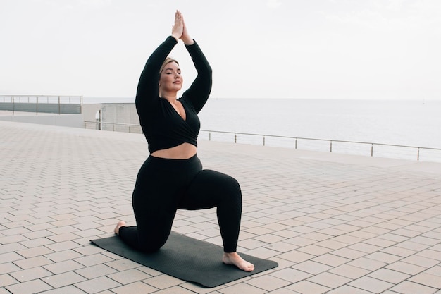 Fille de taille plus pratiquant le yoga devant l'océan un jour d'été