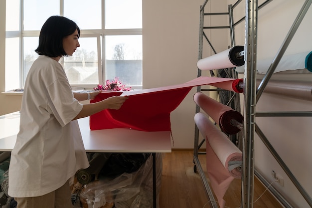 Fille tailleur professionnel choisir un rouleau de tissu pour couper le matériel de mesure de concepteur pour le projet de vêtements