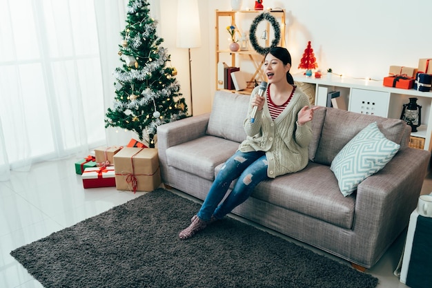 Une fille taïwanaise pleine longueur passe les vacances de Noël à chanter du koraoke. une femme assise dans la salle décorée avec microphone fait la fête toute seule. style de vie authentique