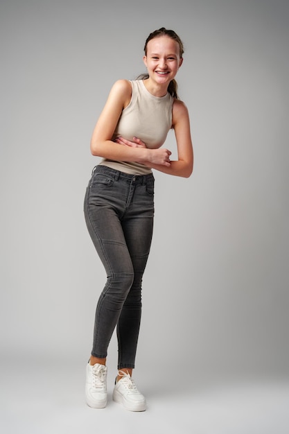 Une fille en tank top beige et un jean gris sur un fond gris