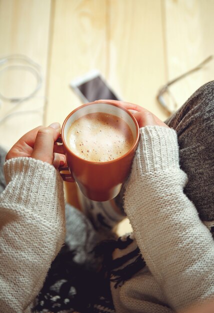 Fille avec une tasse de café assis sur un plancher en bois