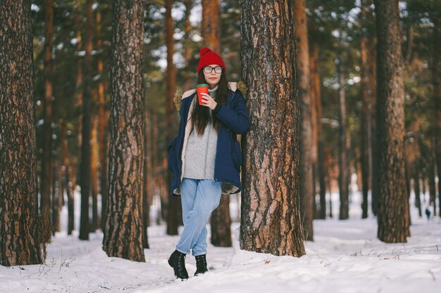 Fille avec une tasse de papier près de l'arbre regarde au loin