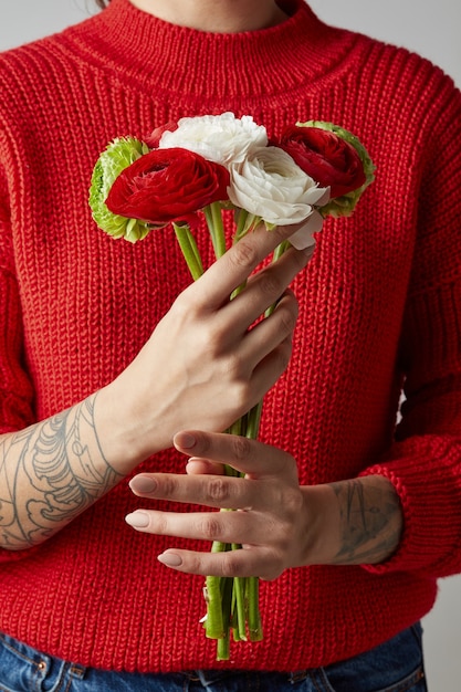 fille avec un tatouage sur les mains dans un pull en tricot rouge tient un bouquet de fleurs. une joyeuse Saint Valentin