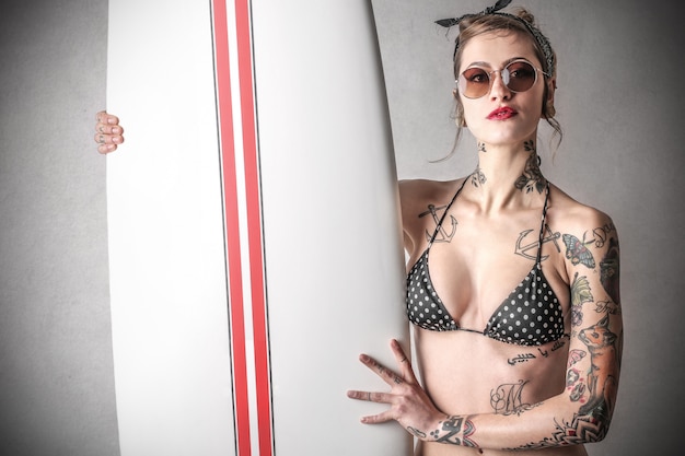 Fille tatouée élégante avec une planche de surf