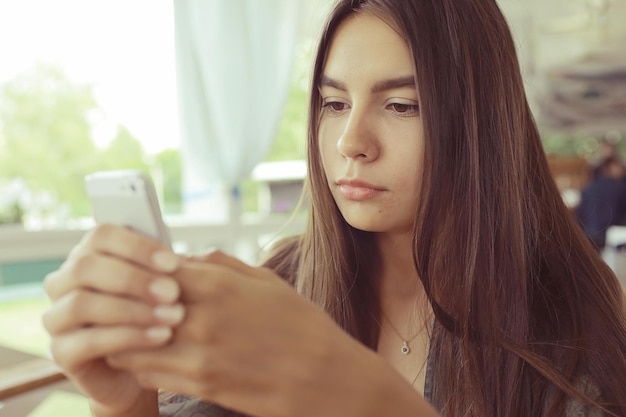 Une fille avec un téléphone dans un café en été.