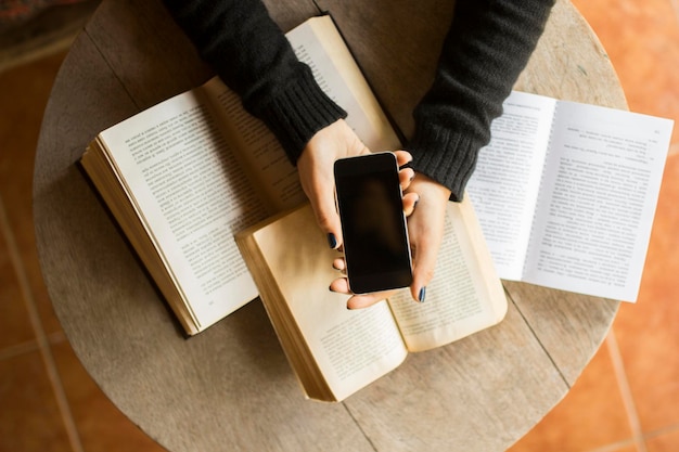 Fille avec téléphone portable et livres sur une table en bois