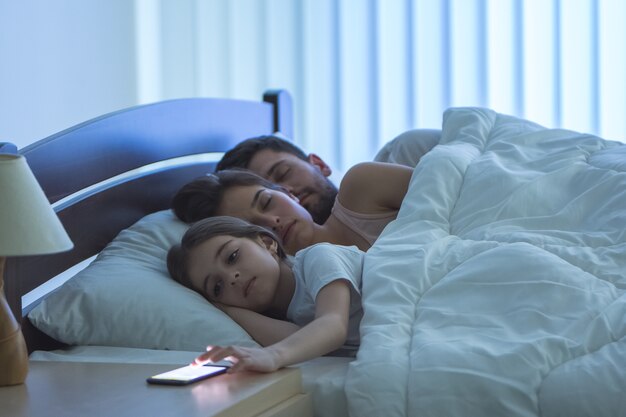 La fille téléphone près des parents endormis sur le lit