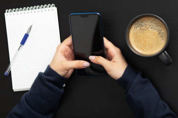 Fille avec un téléphone à la table avec du café et des affaires de maquette de bloc-notes