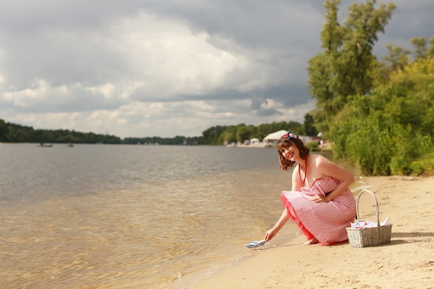 Photo fille tenant un bateau en papier au bord de la rivière en été