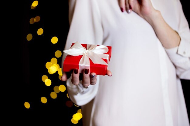 Fille tenant un beau cadeau pour la Saint Valentin. boîte rouge et arc blanc et bokeh en arrière-plan