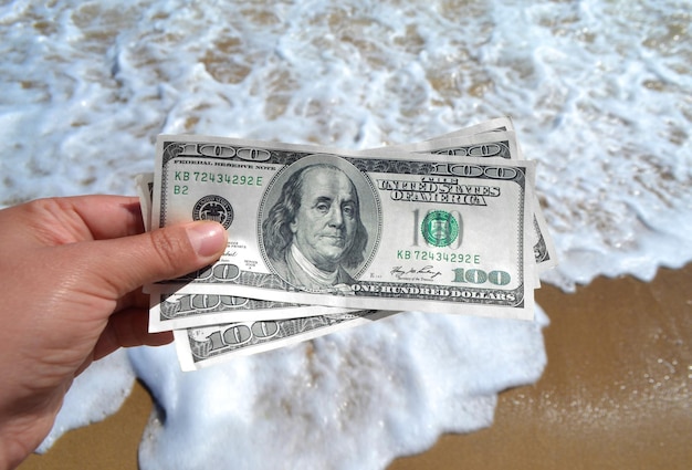 Fille tenant un billet de dollars sur fond de vagues de la mer