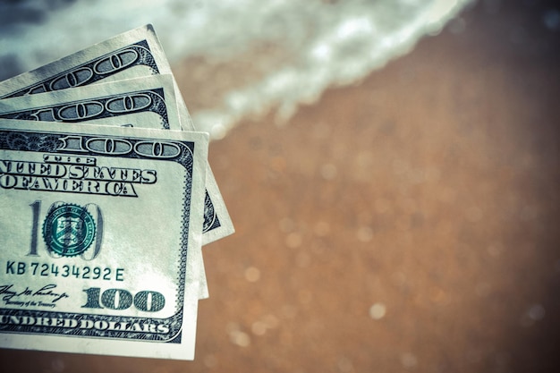 Fille tenant un billet de dollars sur fond de vagues de l'océan de mer avec mousse blanche et bea humide de sable