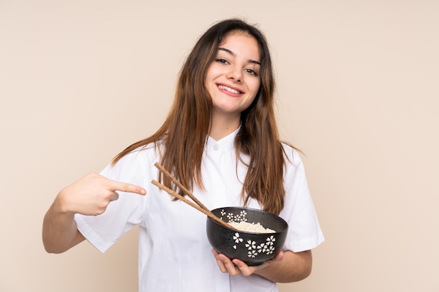 Fille tenant un bol plein de nouilles sur le mur et en le pointant