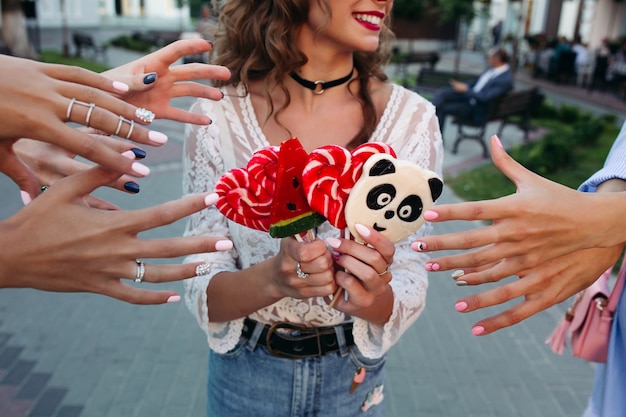 fille tenant des bonbons sur le bâton et les mains de trois filles qui s'étire les mains pour prendre des bonbons.