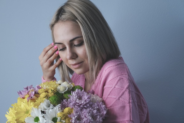 Fille tenant un bouquet de fleurs dans ses mains. Fond clair, portrait en gros plan. Concept de vacances, anniversaire, journée de la femme.