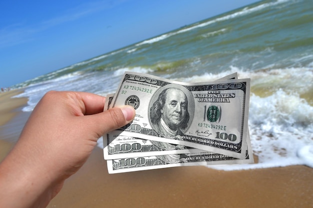 Fille tenant une facture d'argent de 300 dollars sur fond de vagues de la mer