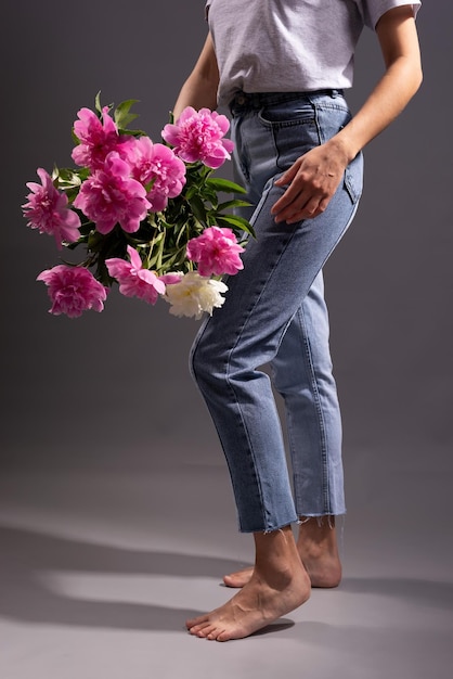 Fille tenant des fleurs en pantalon denim, sur fond gris.