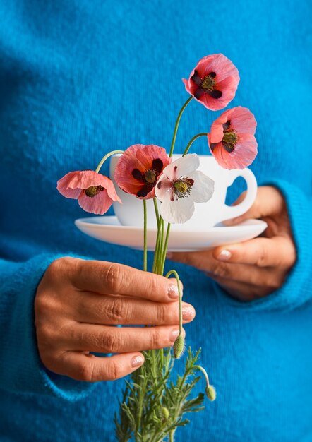 Fille tenant des fleurs de pavot et une tasse blanche de café chaud du matin. Fond bleu.