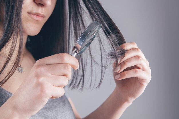 Fille tenant une loupe dans sa main et examine ses cheveux