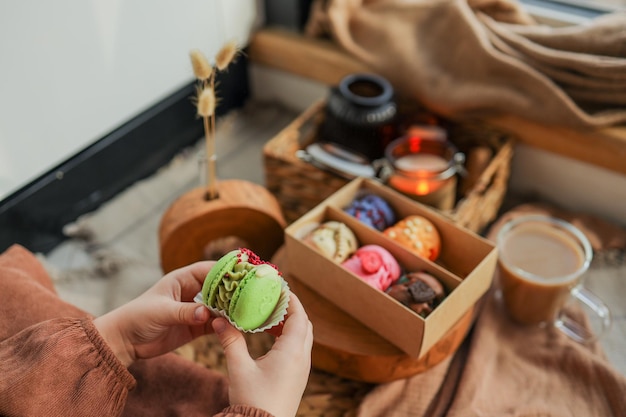 Fille tenant un macaron à la main avec une boîte de macarons assortis en arrière-plan dans une atmosphère chaleureuse et chaleureuse