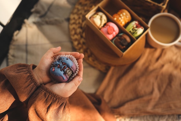 Fille tenant un macaron à la main avec une boîte de macarons assortis en arrière-plan dans une atmosphère chaleureuse et chaleureuse