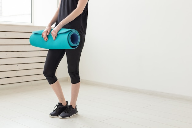 Fille tenant en main un tapis de sport posant sur une classe blanche