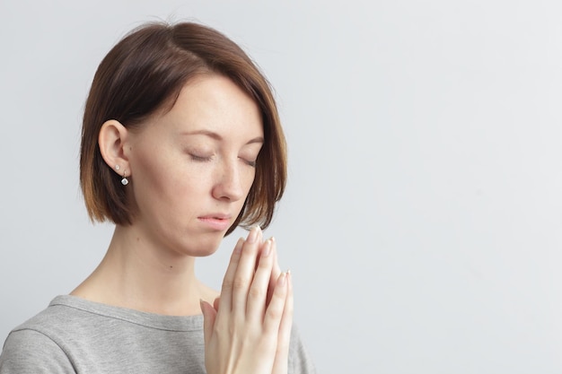 Fille tenant les mains ensemble coudes sur les côtés Yeux fermés Méditer ou faire un vœu en essayant de se calmer