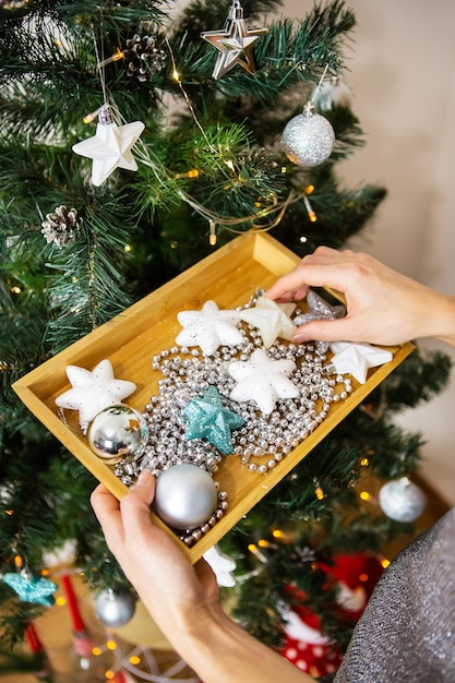 Fille tenant un plateau en bois avec des jouets de noël et décorant un arbre de noël se préparant pour le nouvel an et noël