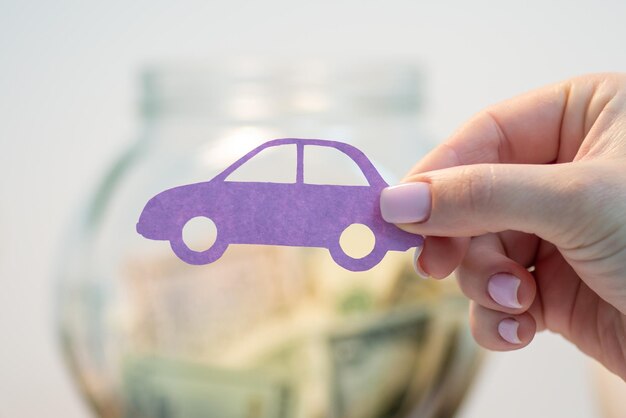 Fille tenant un symbole de voiture en papier contre un bocal en verre avec des économies Économiser de l'argent pour un nouveau concept de voiture