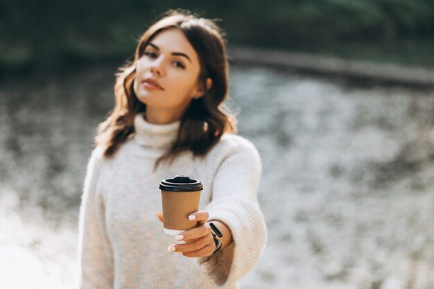 Fille tenant une tasse de café en papier dans le parc sur un hamac